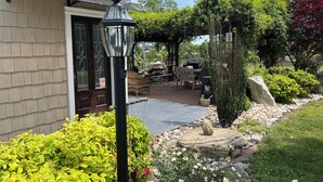 Una casa con un portico coperto, un giardino ricco di piante e un vialetto in pietra.