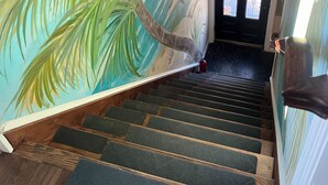 Una scala con un murale tropicale sulle pareti, una ringhiera in legno e un estintore sul pianerottolo.