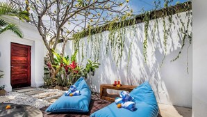 Eine Terrasse mit zwei blauen Sitzgelegenheiten, einer Holzbank und einem kleinen Tisch mit Getränken.