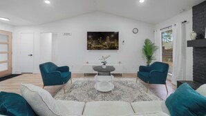 Una sala de estar moderna con un sofá blanco, sillones color turquesa, una mesa redonda con una planta en maceta y un cuadro de un paisaje urbano en la pared.