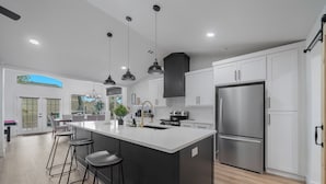 Una cocina moderna con una isla grande, electrodomésticos de acero inoxidable e iluminación colgante.