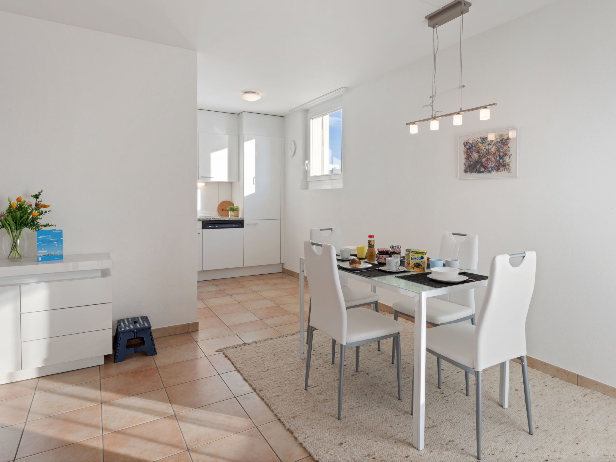 Een moderne keuken met witte kasten, een eettafel met stoelen en een klein krukje.