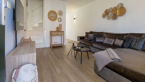 Una sala de estar moderna con piso de madera, un sofá de cuero marrón, una pequeña mesa redonda de centro y un mueble consola de madera con espejo.