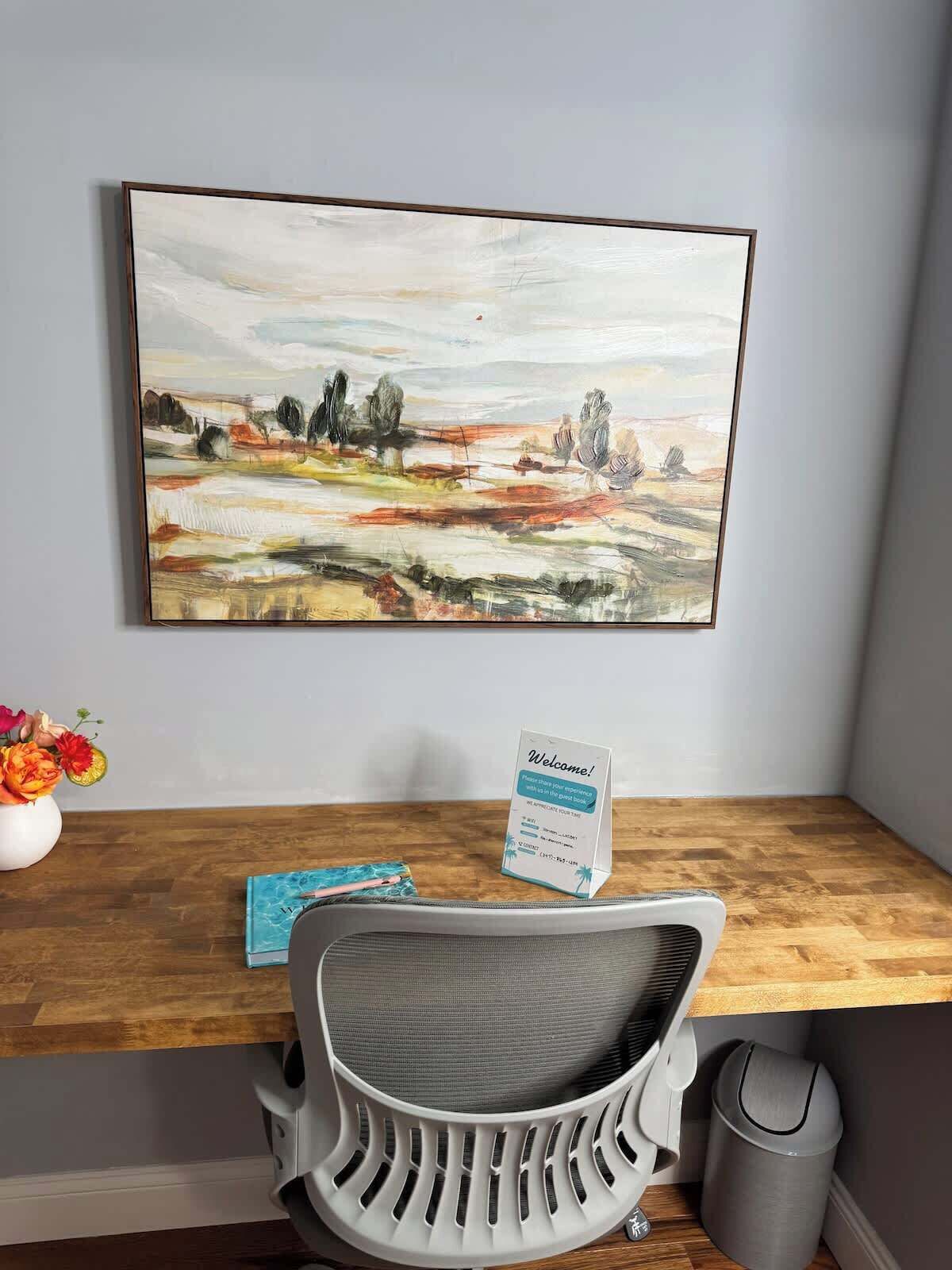 A desk with a chair, a welcome sign, and a painting on the wall.