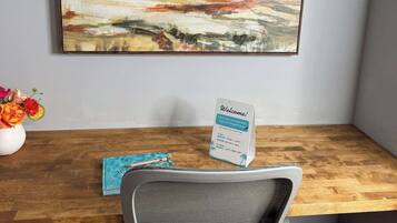 A desk with a chair, a welcome sign, and a painting on the wall.