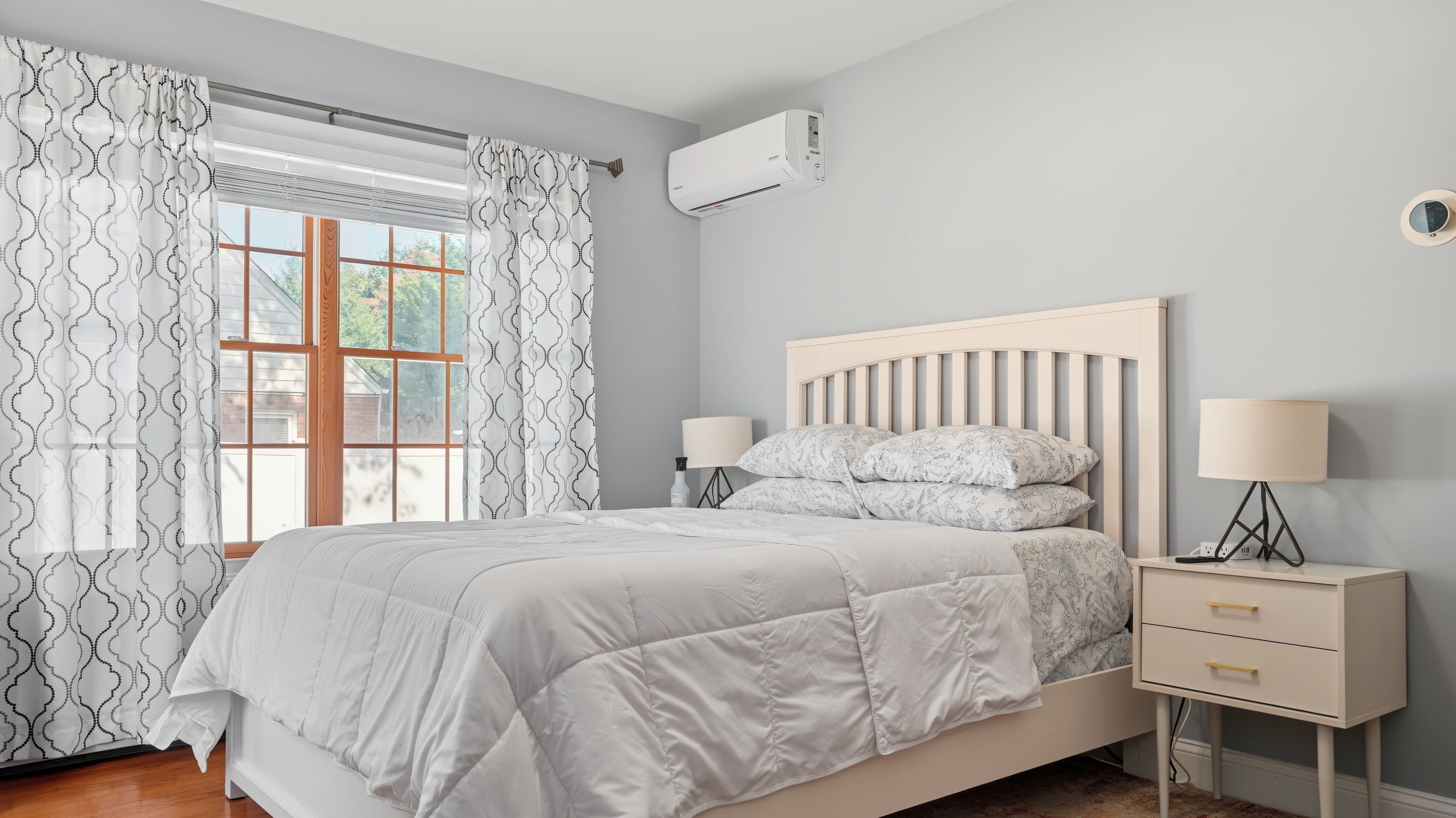 Un dormitorio con cama, lámparas de noche, mesita de noche y ventana con cortinas.
