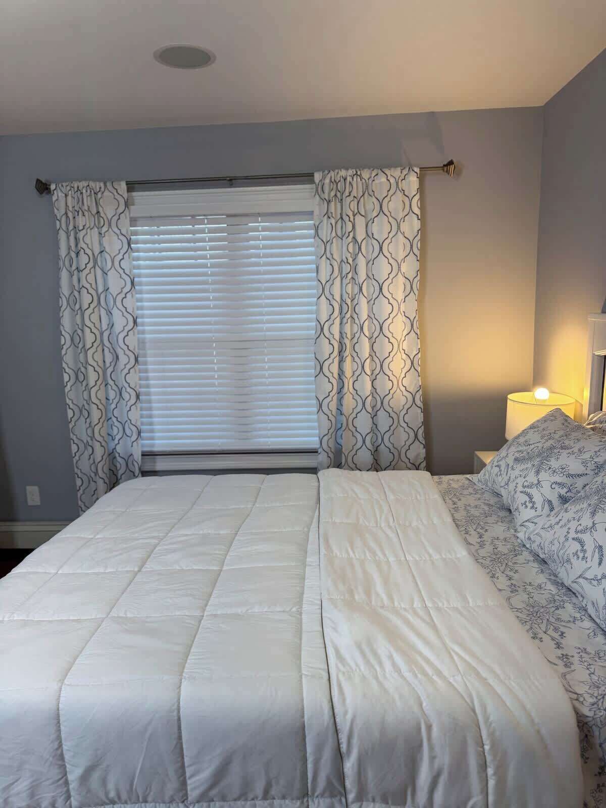 A bedroom with a bed, curtains, a nightstand, and a lamp.