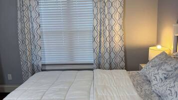 A bedroom with a bed, curtains, a nightstand, and a lamp.