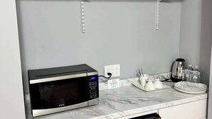 Une cuisine équipée d’un four à micro-ondes encastré, d’un réfrigérateur en acier inoxydable, de meubles blancs et de plans de travail en marbre.