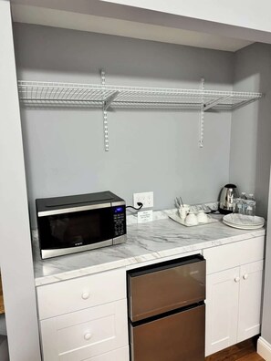 A kitchen with a built-in microwave, stainless steel refrigerator, white cabinets, and marble countertops.