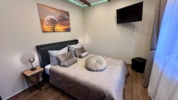 A bedroom with a bed, a nightstand, a painting, a TV, and wooden flooring.