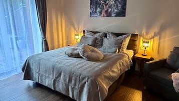 A bedroom with a large bed, two bedside tables with lamps, a painting on the wall, and a view of trees through the window.