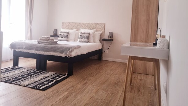 Un dormitorio moderno con cama, mesitas de noche, espejo y suelo de madera.