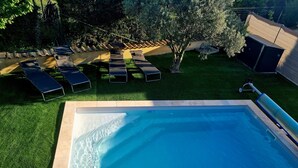 Una piscina rectangular con borde de azulejos, rodeada por un césped cuidado y varias sillas de descanso.