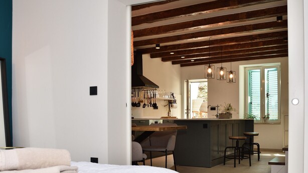A modern bedroom with a large bed, a kitchen area with bar stools, and a view of the outdoors. - Old Town Rovinj Hidden Residence With Terrace (Rovinj)