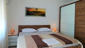 A bedroom with a bed, two bedside tables, a nightstand, a painting, and a wardrobe. - Crikvenica Tranquil and Stylish Apartments With Sea View (Crikvenica)