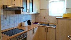 A compact kitchen with wooden cabinets, a gas stove, a sink, and a window with a clock. - Crikvenica Tranquil and Stylish Apartments With Sea View (Crikvenica)