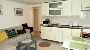 A compact living space with a kitchenette, a sofa with patterned cushions, a small table, and a chair. - Crikvenica Tranquil and Stylish Apartments With Sea View (Crikvenica)