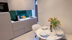 Una cocina moderna con estufa y lavamanos integrados, un comedor con una mesa redonda preparada para dos personas, y un jarrón con tulipanes sobre la mesa.