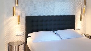 Un dormitorio con cabecera capitonada, cama con ropa blanca e iluminación colgante.
