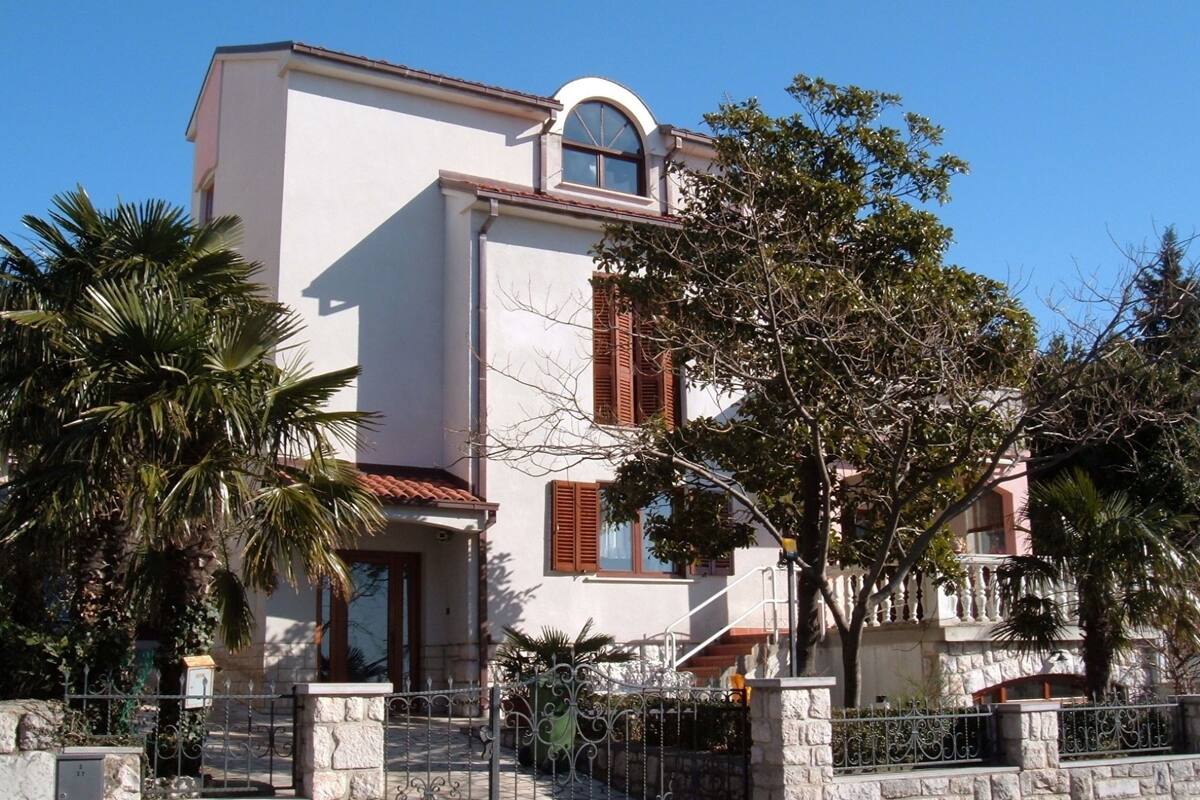 Ein zweistöckiges Gebäude mit weißer Fassade, einem kleinen Rundbogenfenster und einem Balkon.