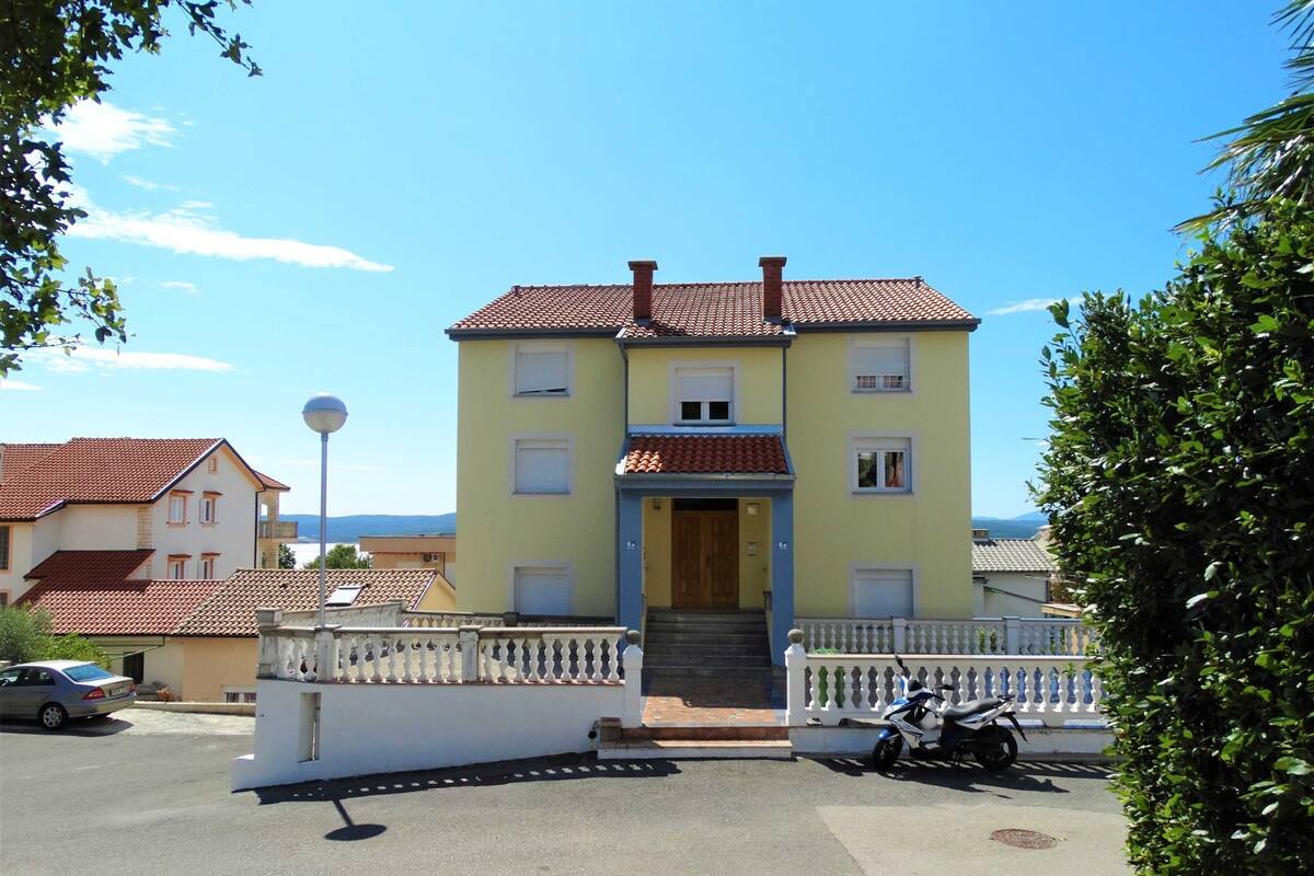 A two-story building with a tiled roof, a front entrance with steps, and a white fence.