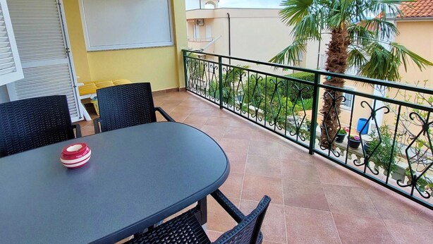 A balcony with a table and chairs, a whiteboard, and a view of a residential area with a palm tree. - Cozy Crikvenica Apartments With Sea View and Balcony (Crikvenica)