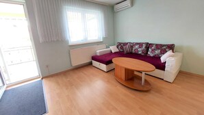 A modern living room with a sofa, a coffee table, and a window with curtains. - Cozy Crikvenica Apartments With Sea View and Balcony (Crikvenica)