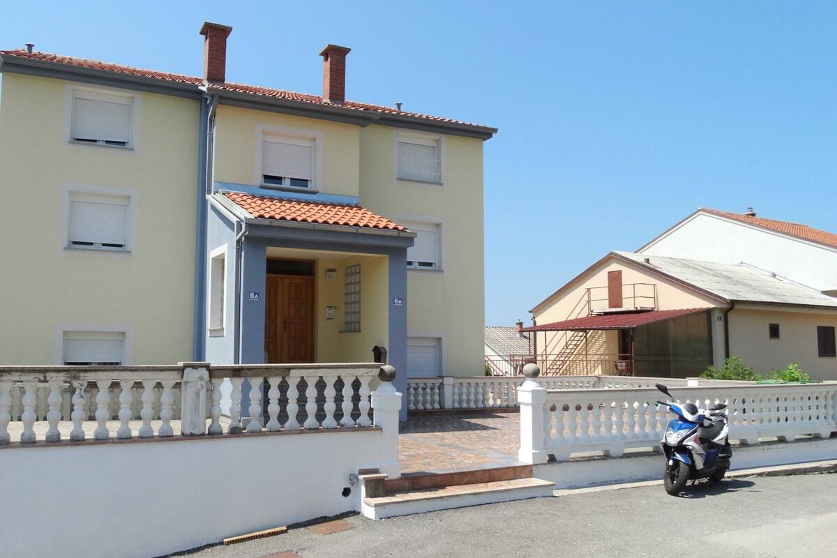 A two-story building with a tiled roof, a balcony with balustrades, and a motorbike parked in front.