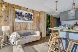 Sala de estar aconchegante com sofá, mesa de centro e espaço bar com banquetas.