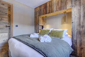 Une chambre à coucher avec une tête de lit en bois, un lit avec une literie blanche, deux oreillers et des serviettes enroulées.