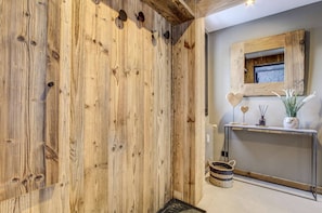 Une pièce aux murs recouverts de lambris en bois, avec un miroir, une console ornée d’objets décoratifs et un panier tressé.