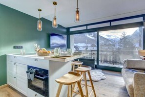 A modern kitchen with a central island, bar stools, a built-in oven, and a large window offering a mountain view. - Luxurious little nest with the best location (MORZINE)