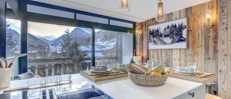 A modern kitchen with a large window, wooden accents, and a view of mountains.