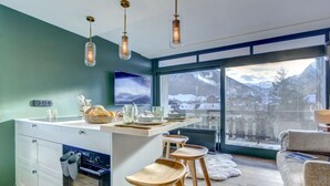 Una cocina moderna con una isla central, taburetes de madera, un amplio ventanal con vistas a la montaña y una zona de estar acogedora.