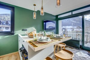 A kitchen with a wooden island, a TV mounted on the wall, and a view of a snowy landscape. - Luxurious little nest with the best location (MORZINE)