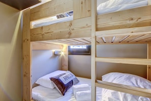 Quarto com beliche, claraboia, travesseiro com texto e luminária fixada na parede.