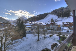 Vila coberta de neve com casas, uma estrada e uma montanha ao fundo.
