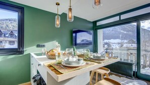 Cocina moderna con una isla central, sillas de madera, un ventanal con vistas a un paisaje nevado y lámparas colgantes.