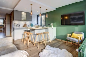 Een moderne keuken met barstoelen, een zithoek met een bank, en een groene accentmuur.