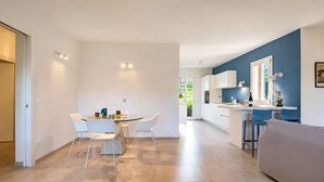 A modern kitchen with white cabinets, a dining area with a round table and chairs, and a living area with a sofa. - Villa Dei Pini, Porto Azzurro (Porto Azzurro)