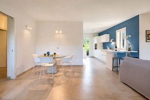 A modern kitchen with white cabinets, a dining area with a round table and chairs, and a living area with a sofa.