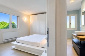 A bedroom with a bed, a window, a radiator, and a bathroom with a sink. - Villa Dei Pini, Porto Azzurro (Porto Azzurro)