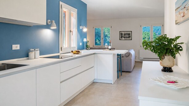 A modern kitchen with white cabinets, a blue accent wall, and a view of the outdoors. - Villa Dei Pini, Porto Azzurro (Porto Azzurro)