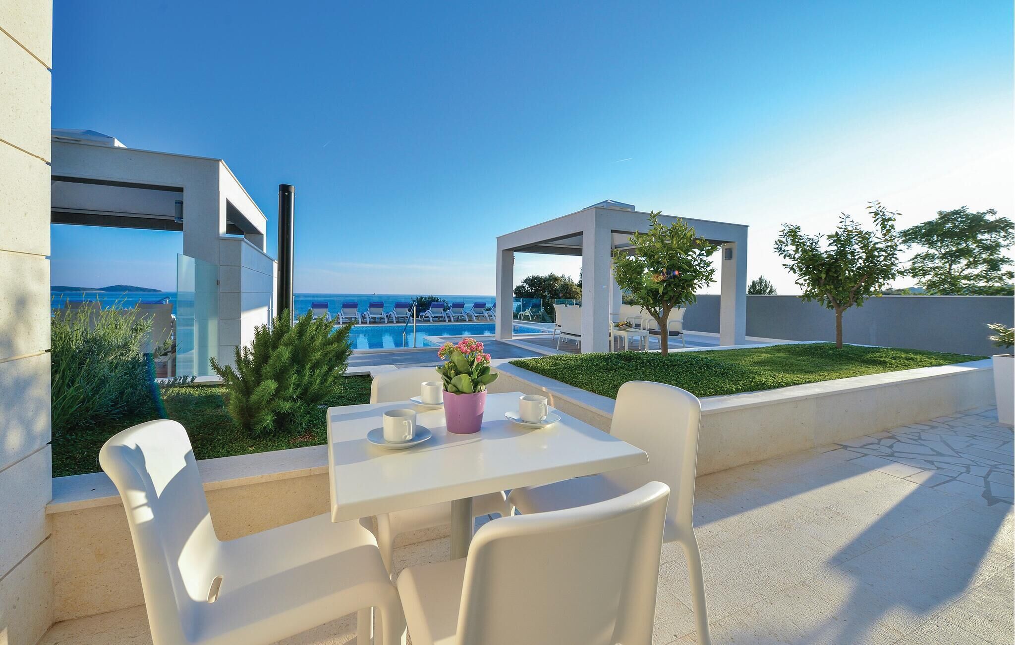 A modern outdoor seating area with a pool view, white furniture, and a clear sky.