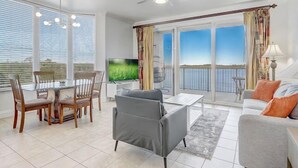 A modern living room with a dining area, a flat-screen TV, and a balcony with a view. - Newly Renovated! 2-Bedroom 2-Bath Stunning LakeView at Blue Heron Beach Resort (Orlando)