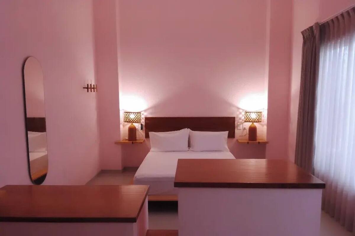 Quarto de hotel com cama, abajures, um espelho e uma mesa de cabeceira de madeira.