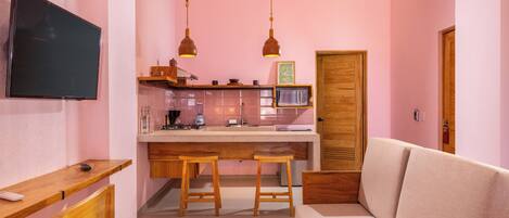 Un espace de vie compact comprenant un coin cuisine, un téléviseur à écran plat fixé au mur, des meubles en bois et un canapé.
