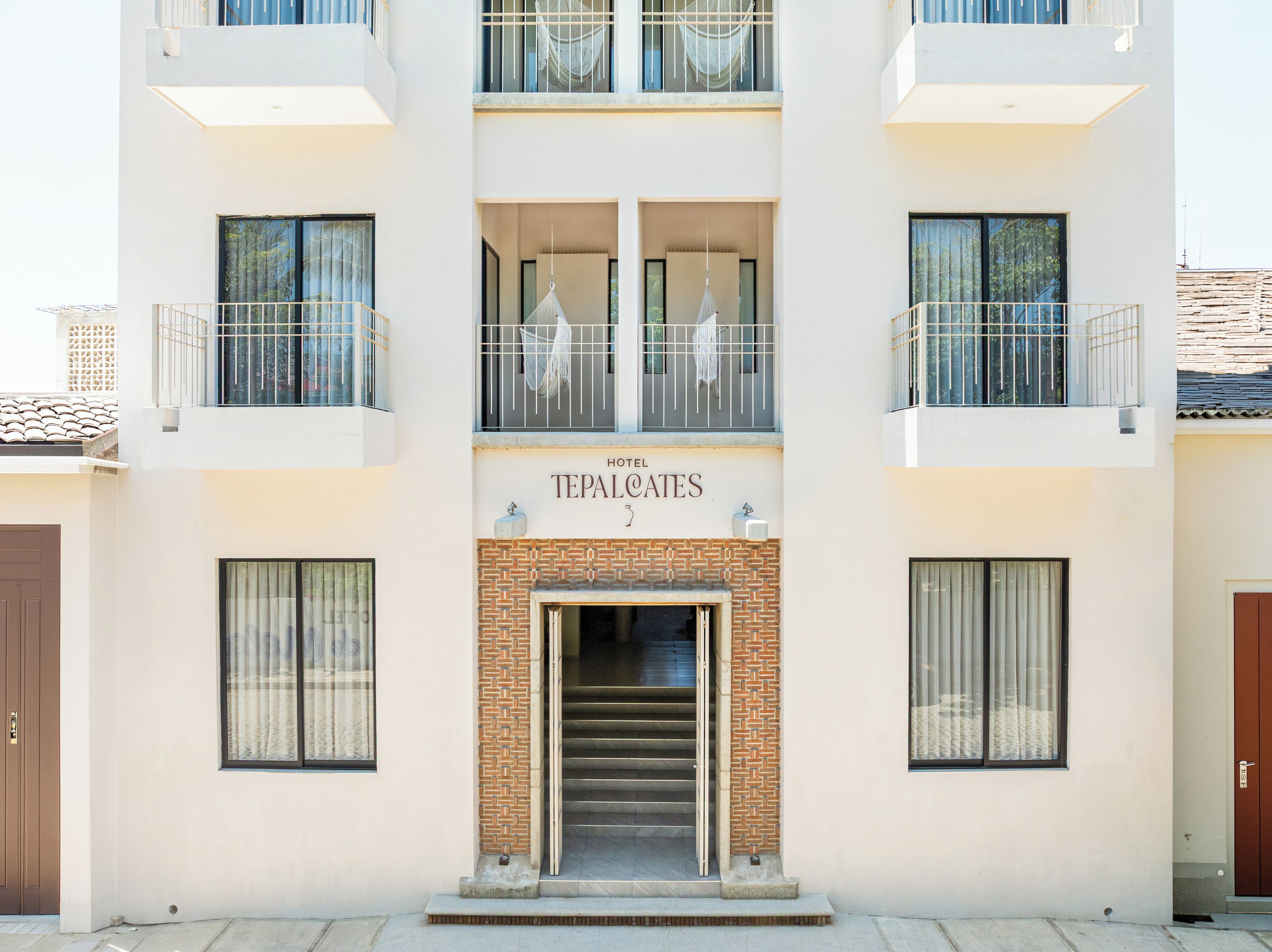 Un hotel llamado 'TEPALCAITES' con una fachada moderna, varios balcones y una entrada central con una escalera.