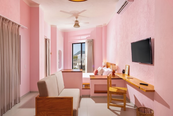 Una habitación con cama, escritorio, silla, televisor y ventana con cortinas.